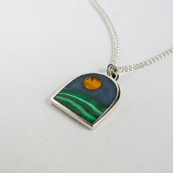 Necklace with a pendant featuring a moon over hill design on a white background