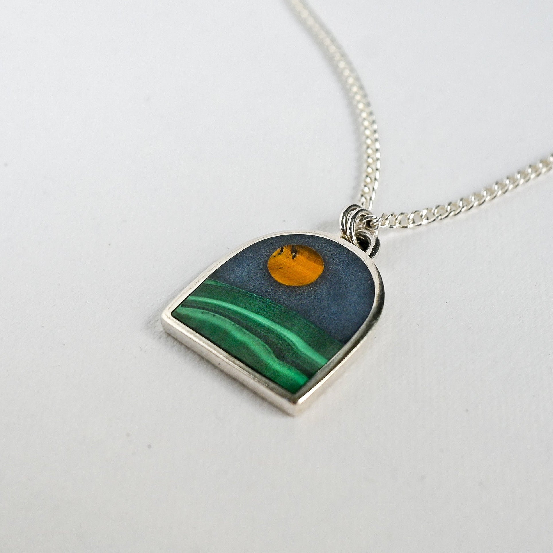 Necklace with a pendant featuring a moon over hill design on a white background