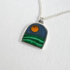 Necklace with a pendant featuring a yellow moon over a green mountain on a white background