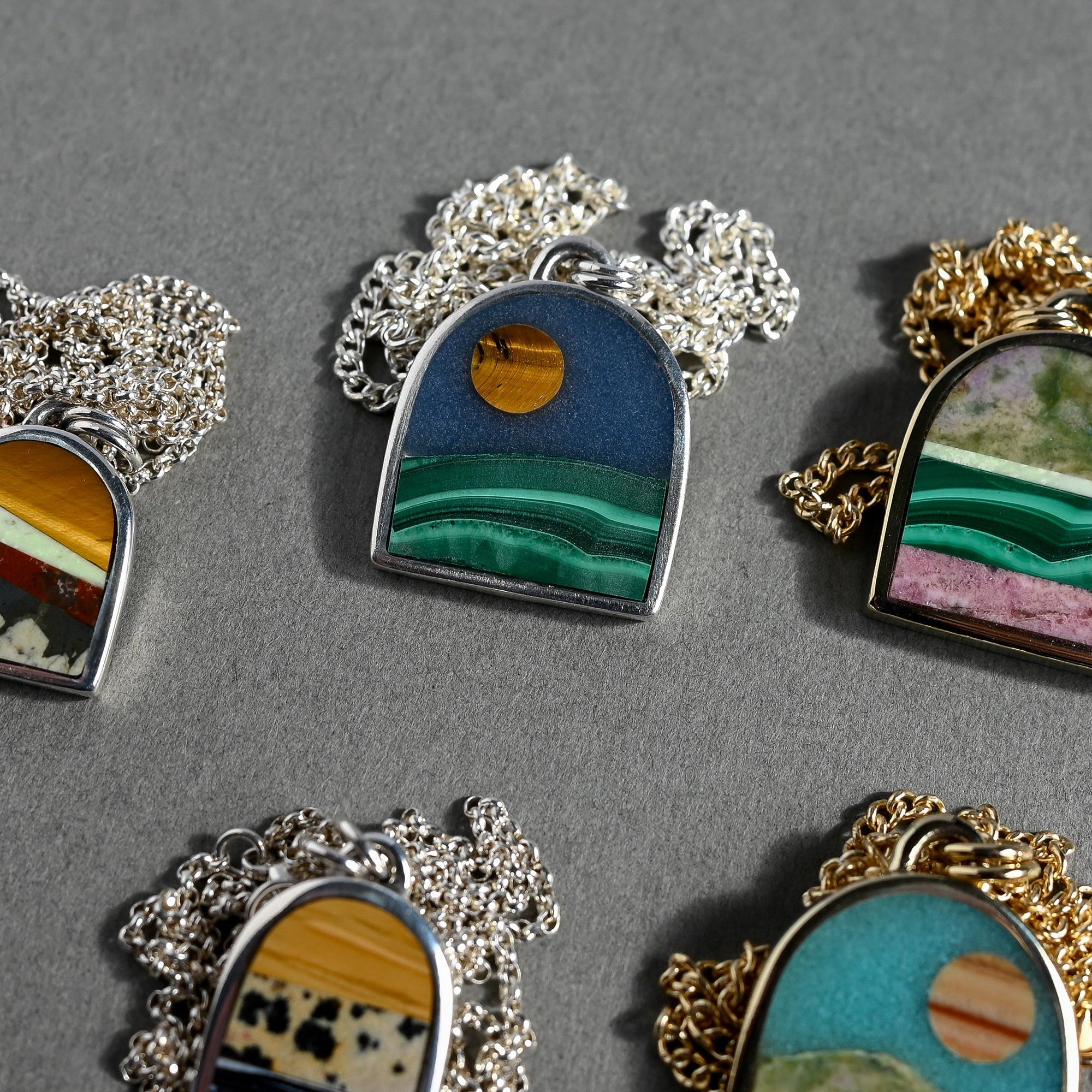 Collection of miniature landscapes in pendant form on a gray background