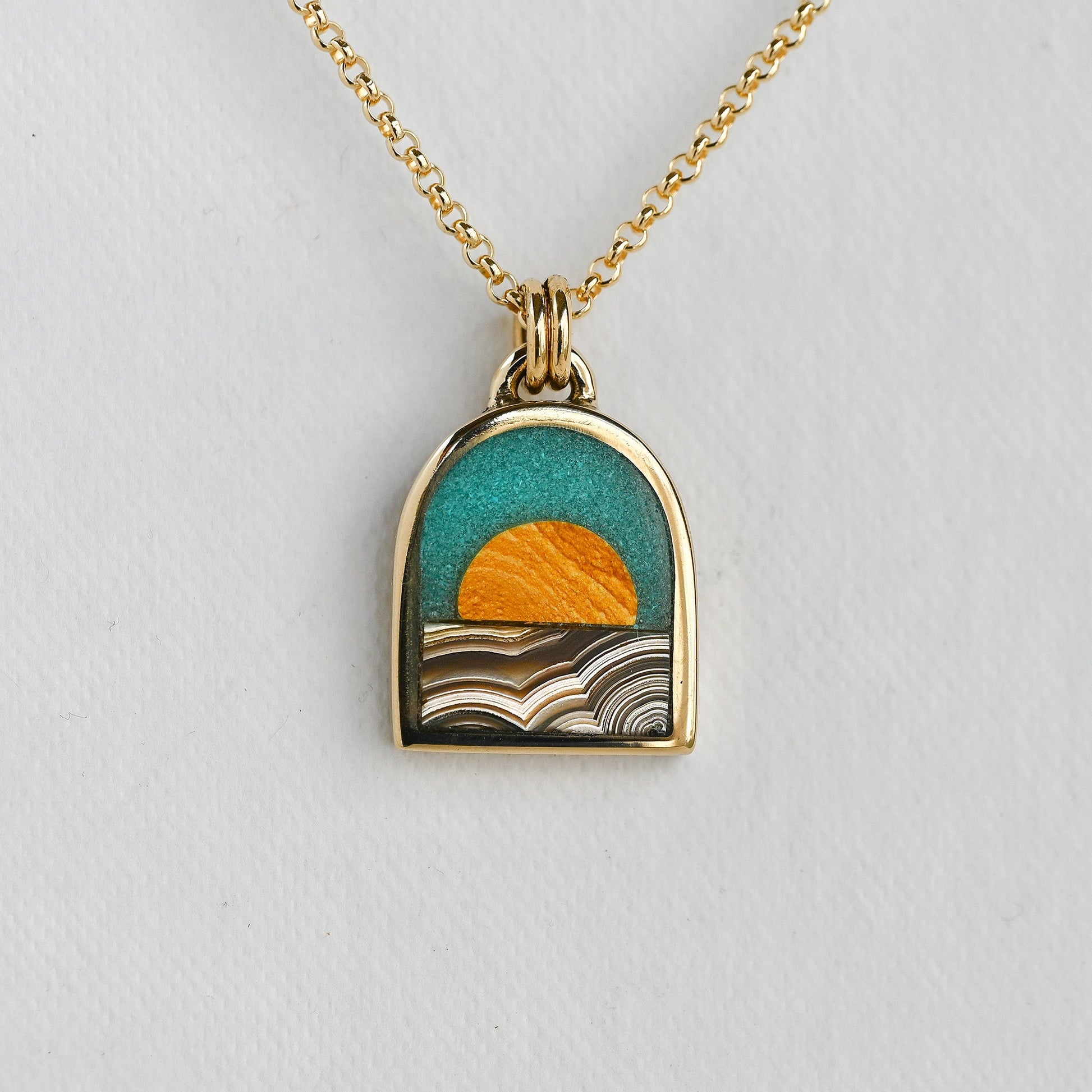 Gold necklace with a pendant featuring a sunset design on a light gray background