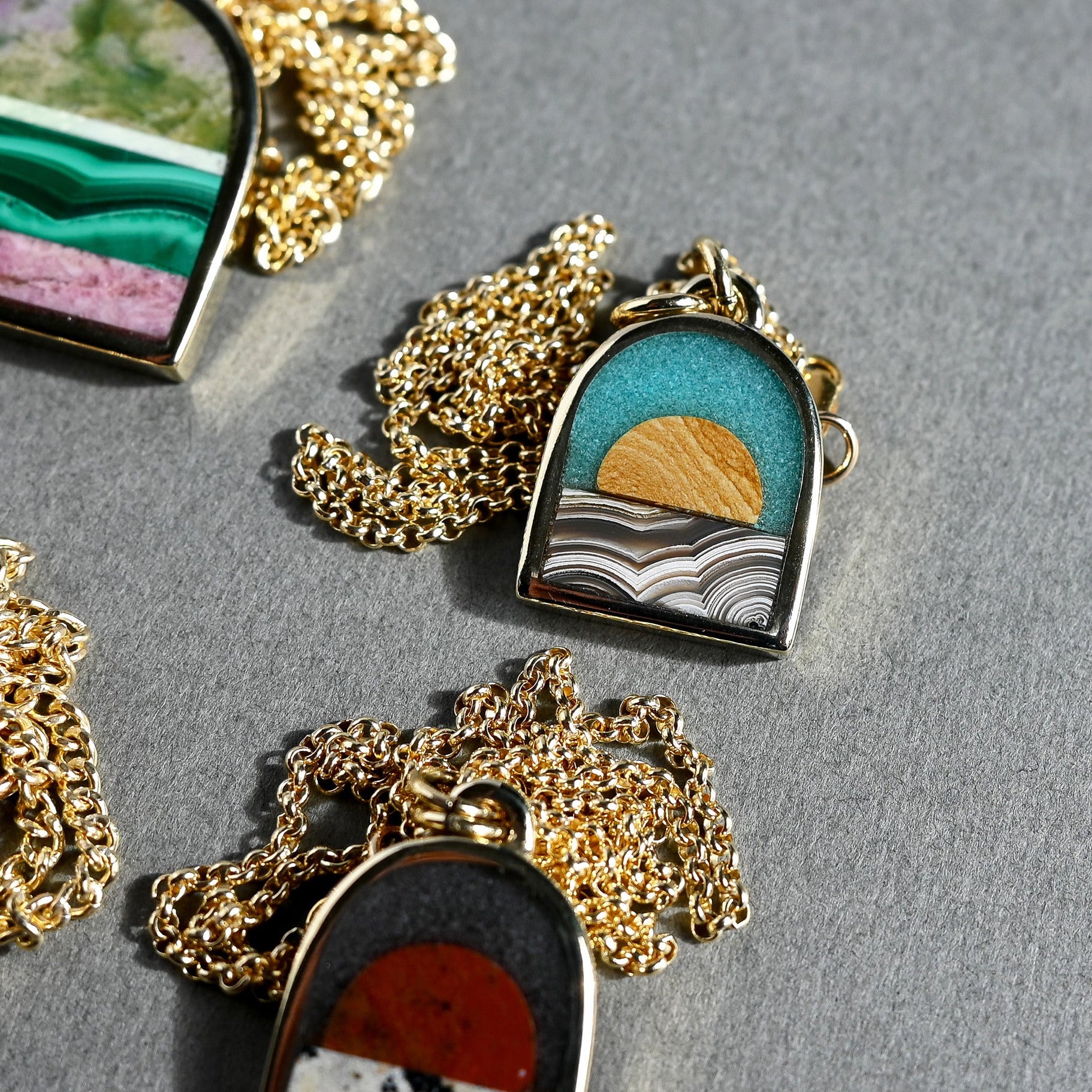Colorful necklaces with scenic pendants on a gray surface