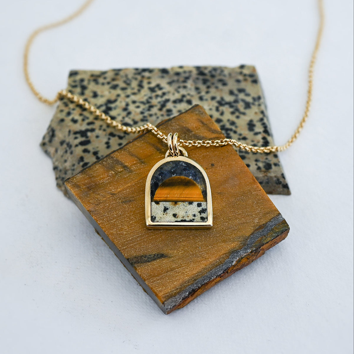 Gold pendant necklace featuring a tiger's eye sun, a spotted dalmatian stone bottom and a dark blue lapis sky