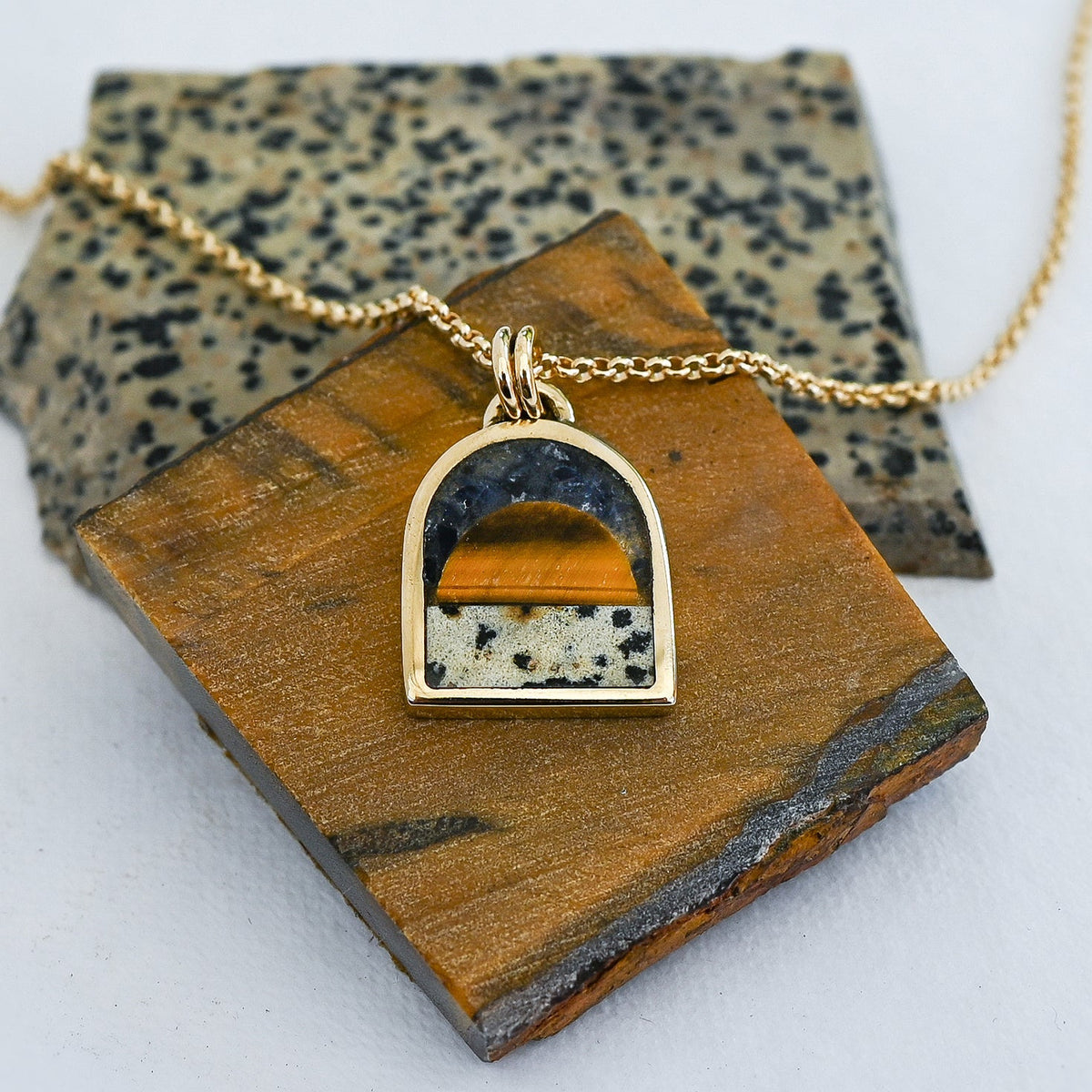 Gold pendant necklace featuring a tiger's eye sun, a spotted dalmatian stone bottom and a dark blue lapis sky