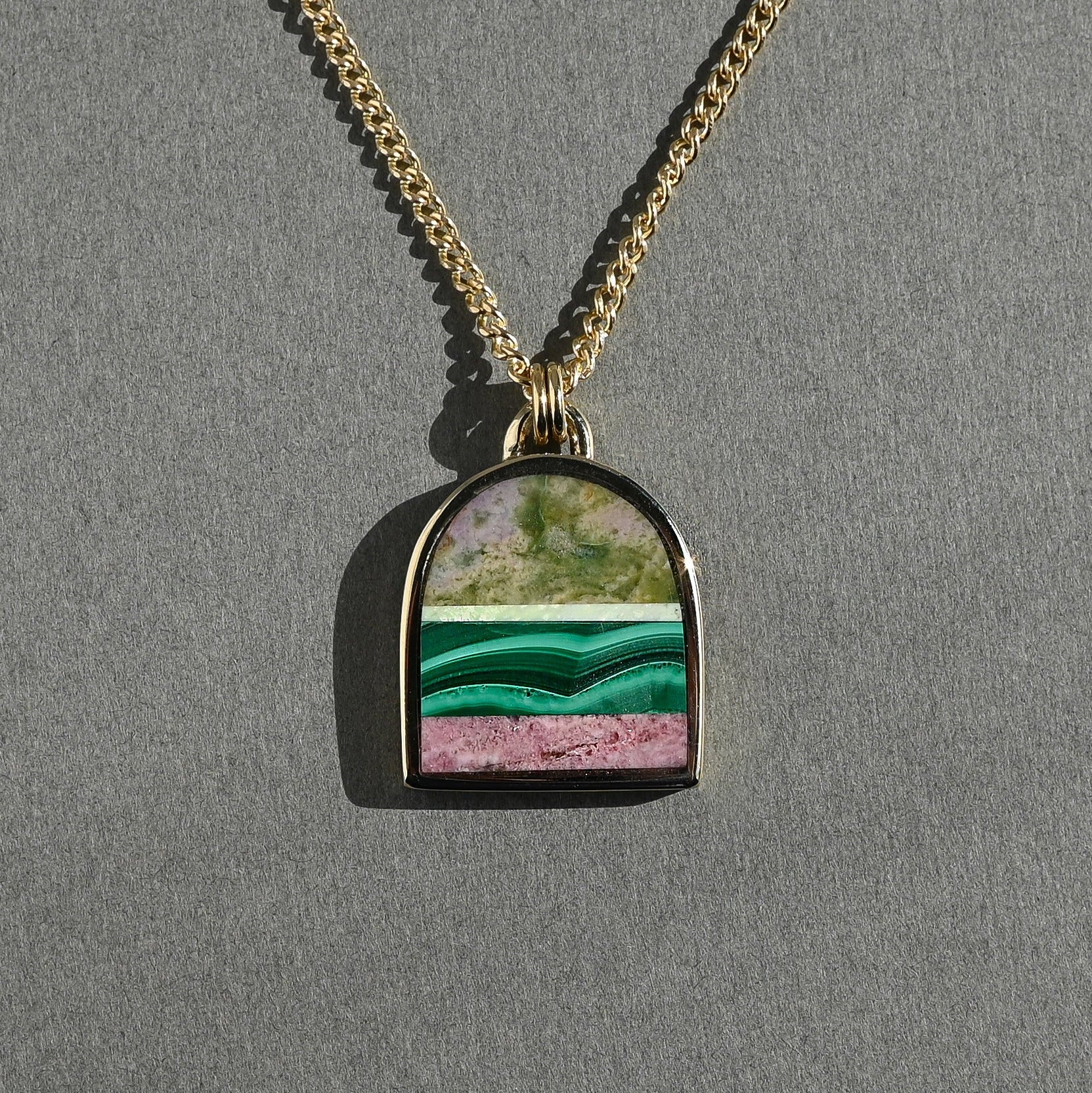 Necklace with a pendant featuring a green and pink stone on a gray background