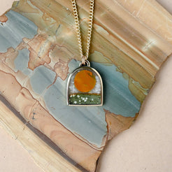 arch shaped gold pendant featuring a stone sun design on a stone backdrop