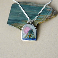 silver arch-shaped necklace with a pink, green and blue stones depicting a landscape scene.