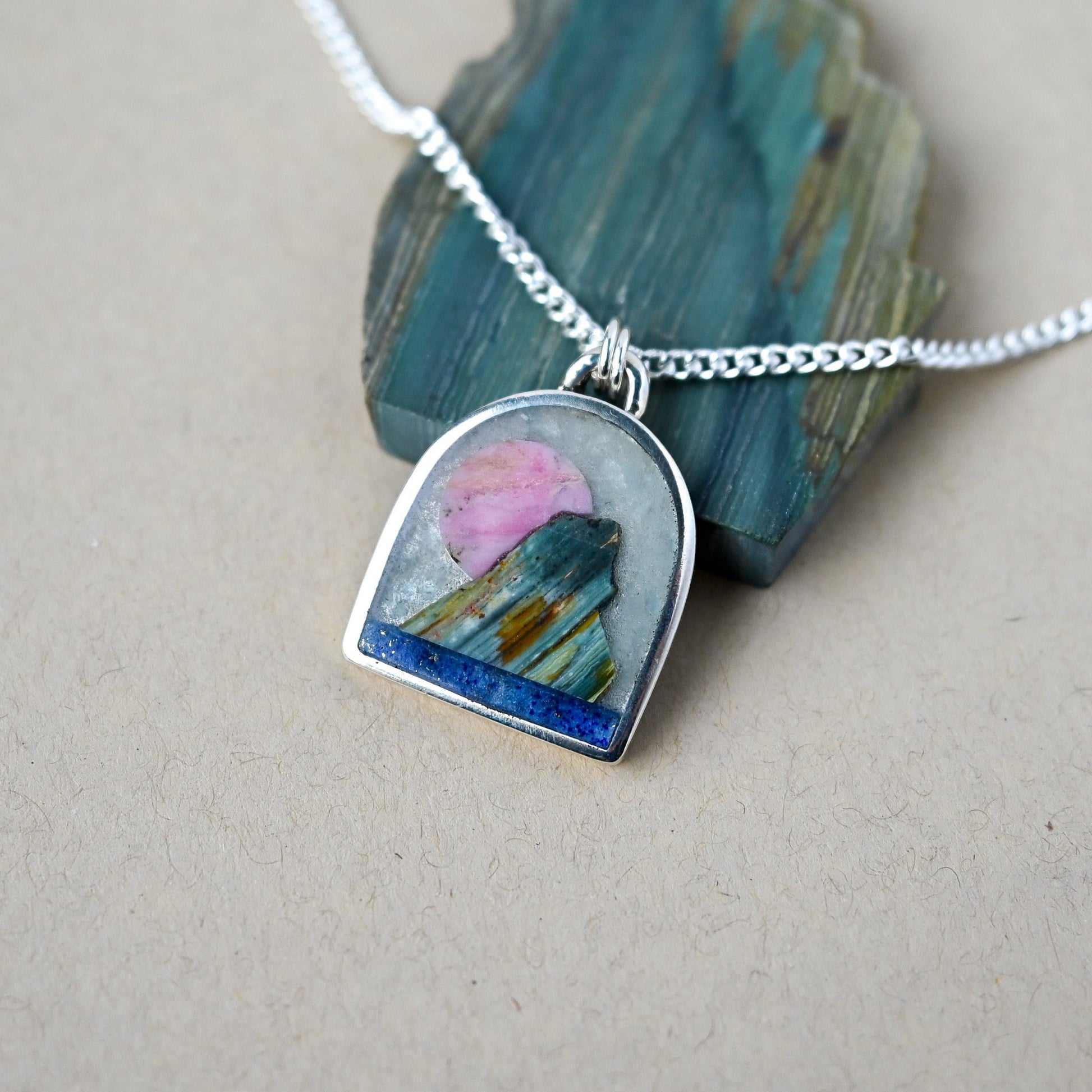 Necklace with a pendant featuring a pink and blue design, displayed on a stone.