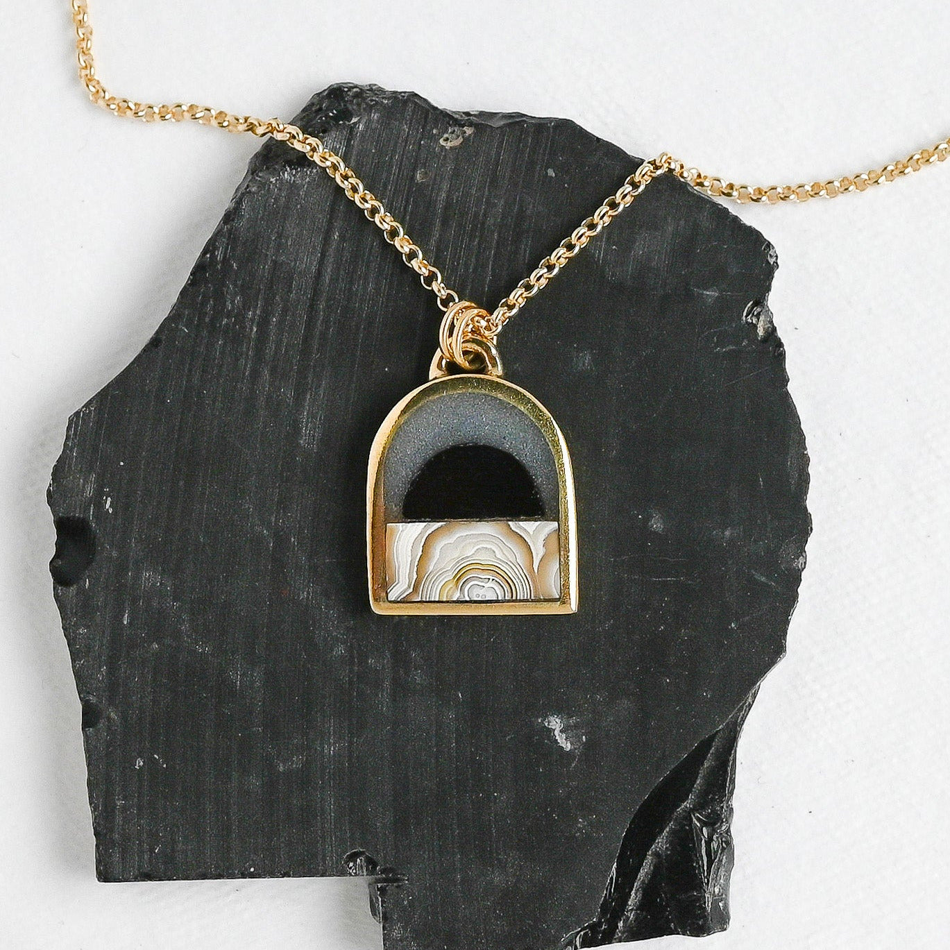 gold arch-shaped pendant with a stone landscape design on a black stone slab
