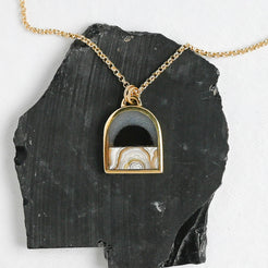 gold arch-shaped pendant with a stone landscape design on a black stone slab