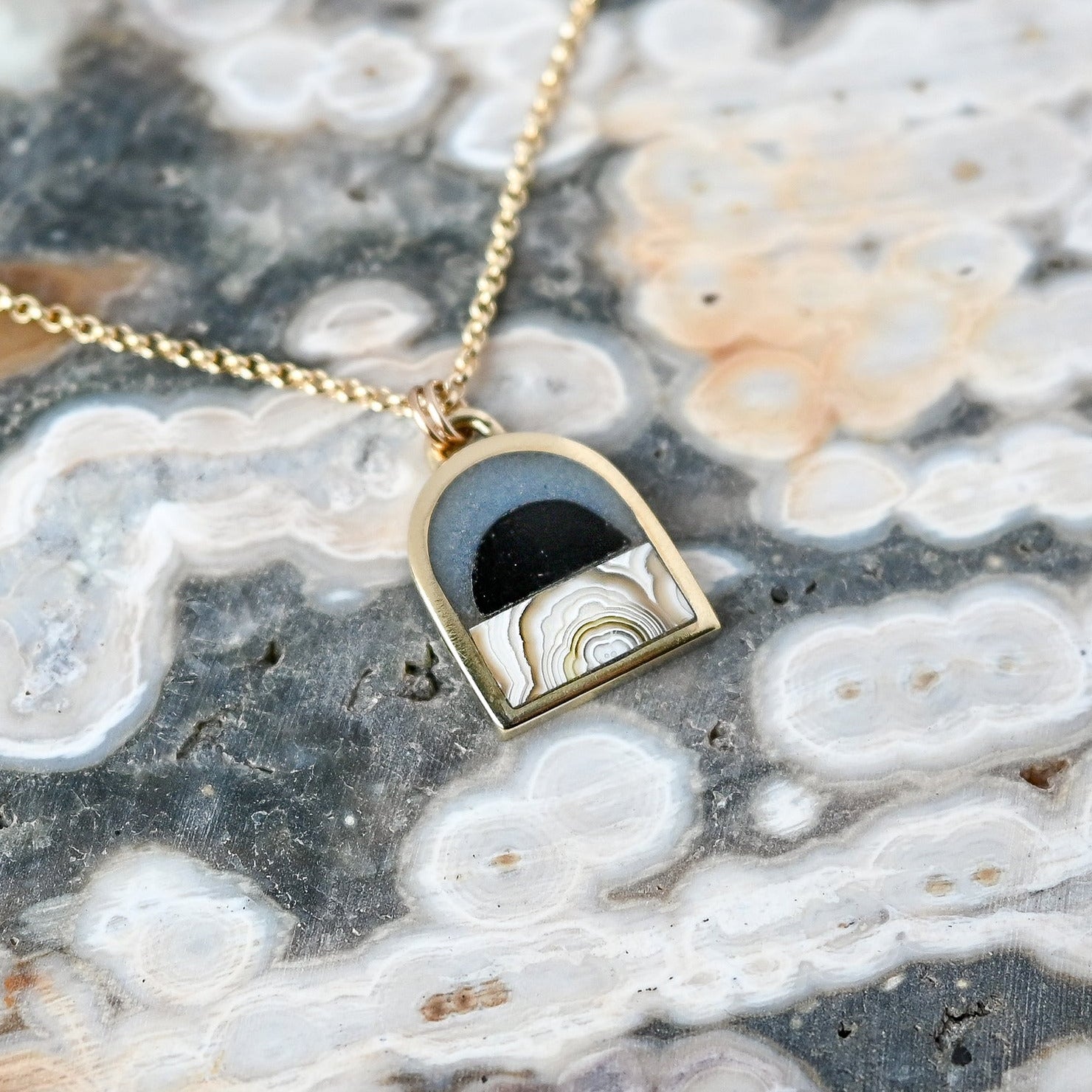 Gold necklace with a pendant on a textured stone surface