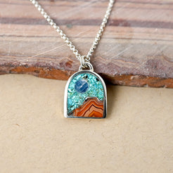 silver necklace with arch shaped pendant depicting a landscape made of stones