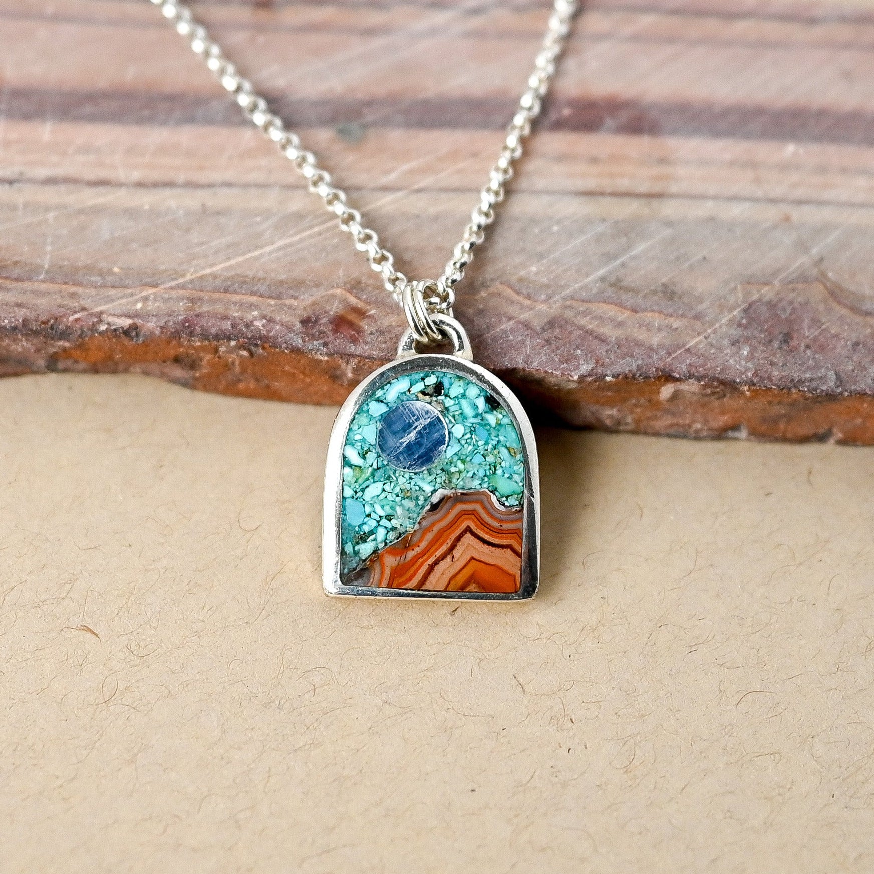 silver necklace with arch shaped pendant depicting a landscape made of stones