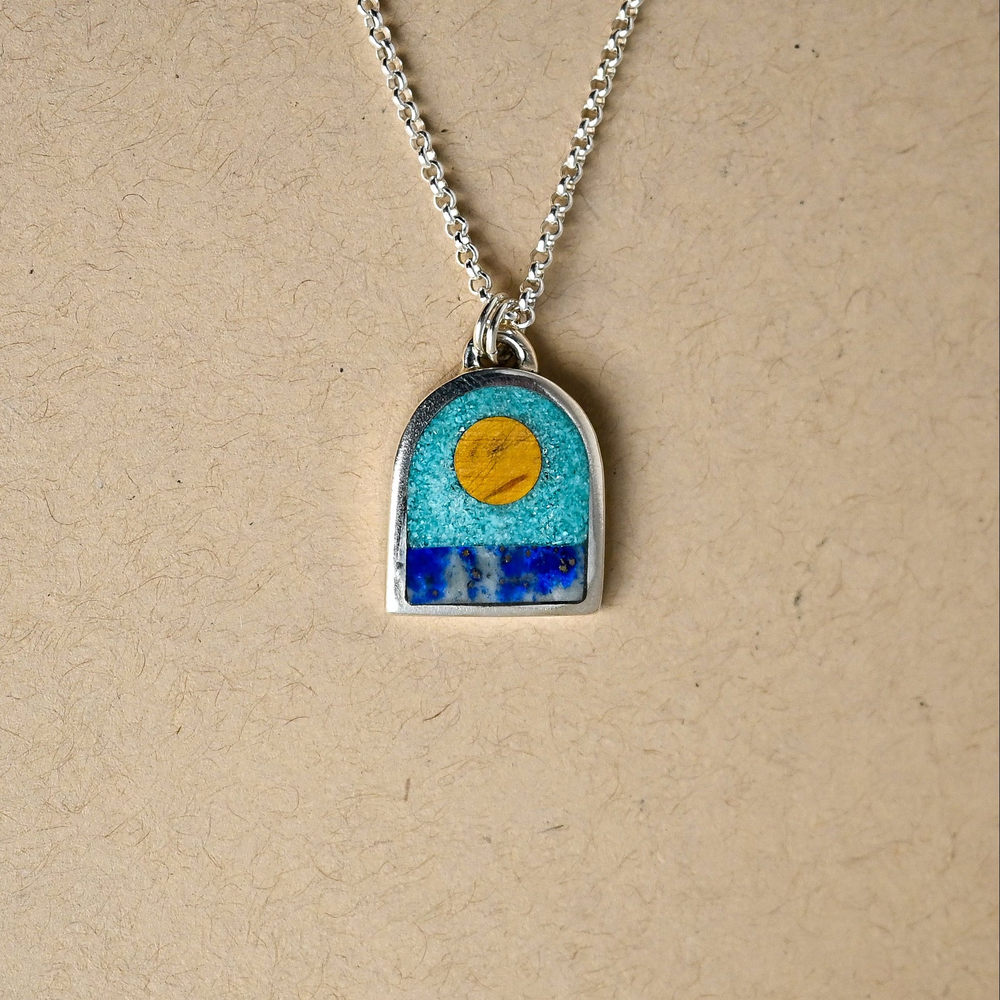 Necklace with a pendant featuring a blue sky and sun design on a beige background