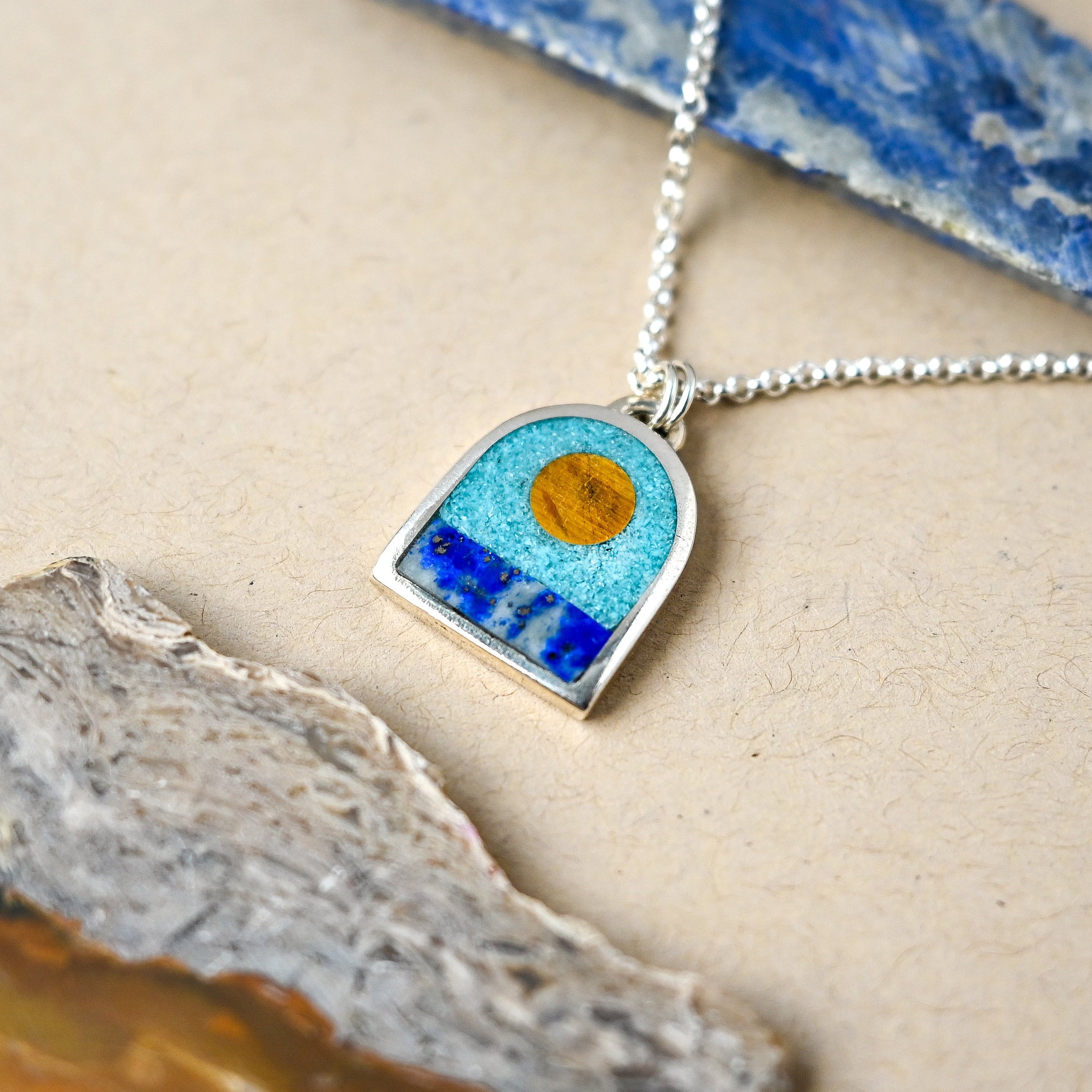 Necklace with a arch shaped pendant featuring blue and orange design on a textured surface.