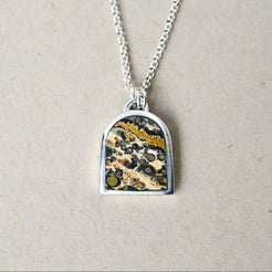 sterling silver necklace with an arch shaped pendant featuring leopard skin jasper stone on a beige background