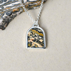 sterling silver necklace with an arch shaped pendant featuring leopard skin jasper stone on a beige background