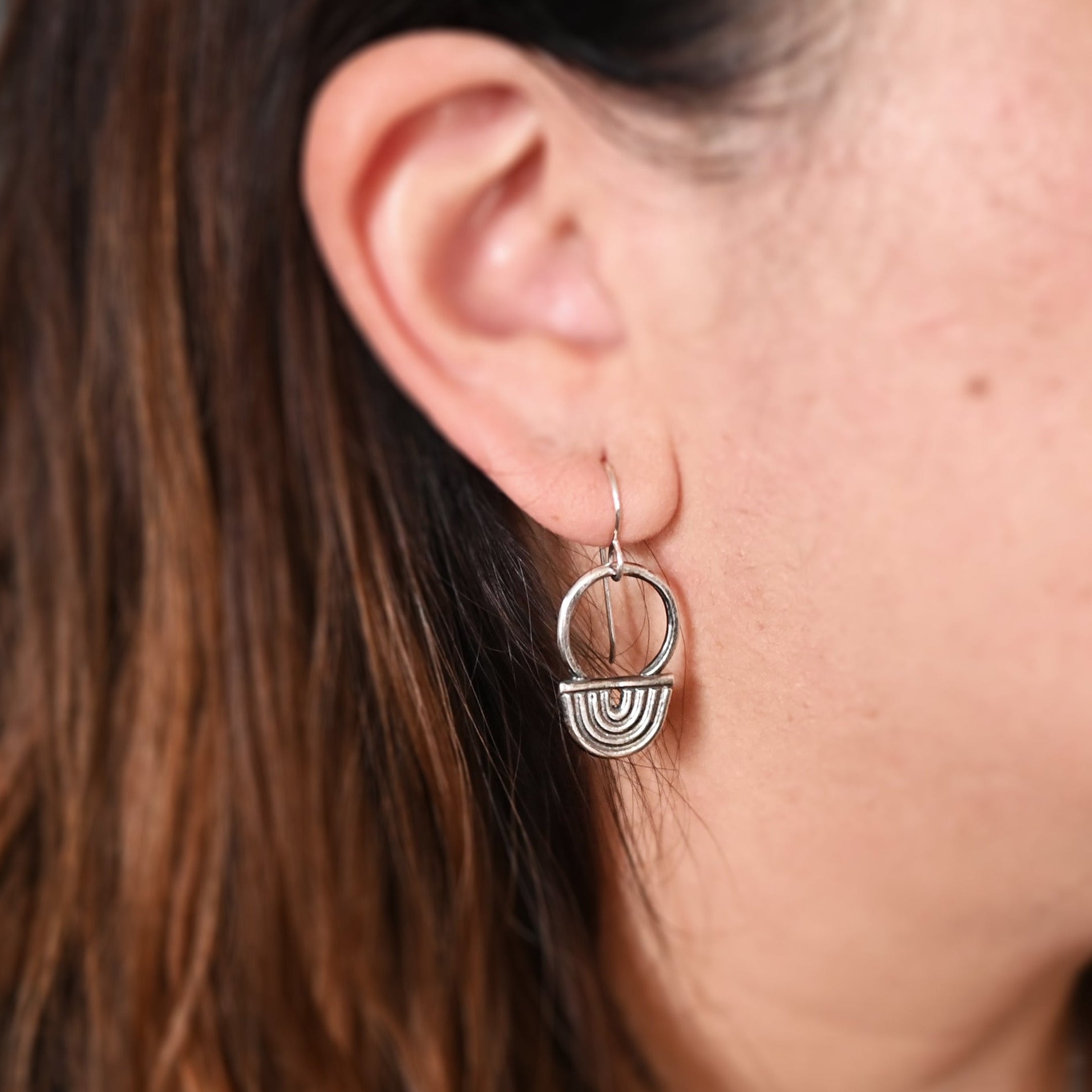 Close-up of an ear wearing a silver earring with a geometric design.