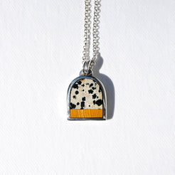 A silver chain necklace with an arched pendant featuring a black-and-white cow print top and a textured orange bottom, displayed on a white background.
