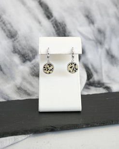 Pair of silver earrings with circular designs featuring dalmatian stone on a white card against a fabric background