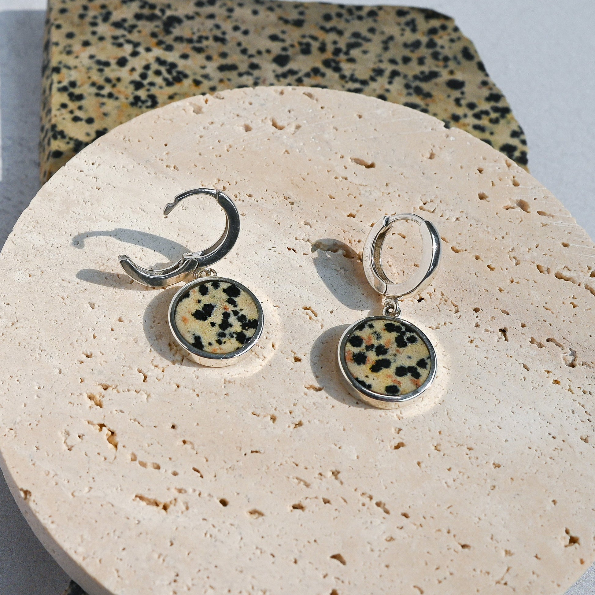 Pair of earrings with dalmatian jasper stones on a round stone surface.