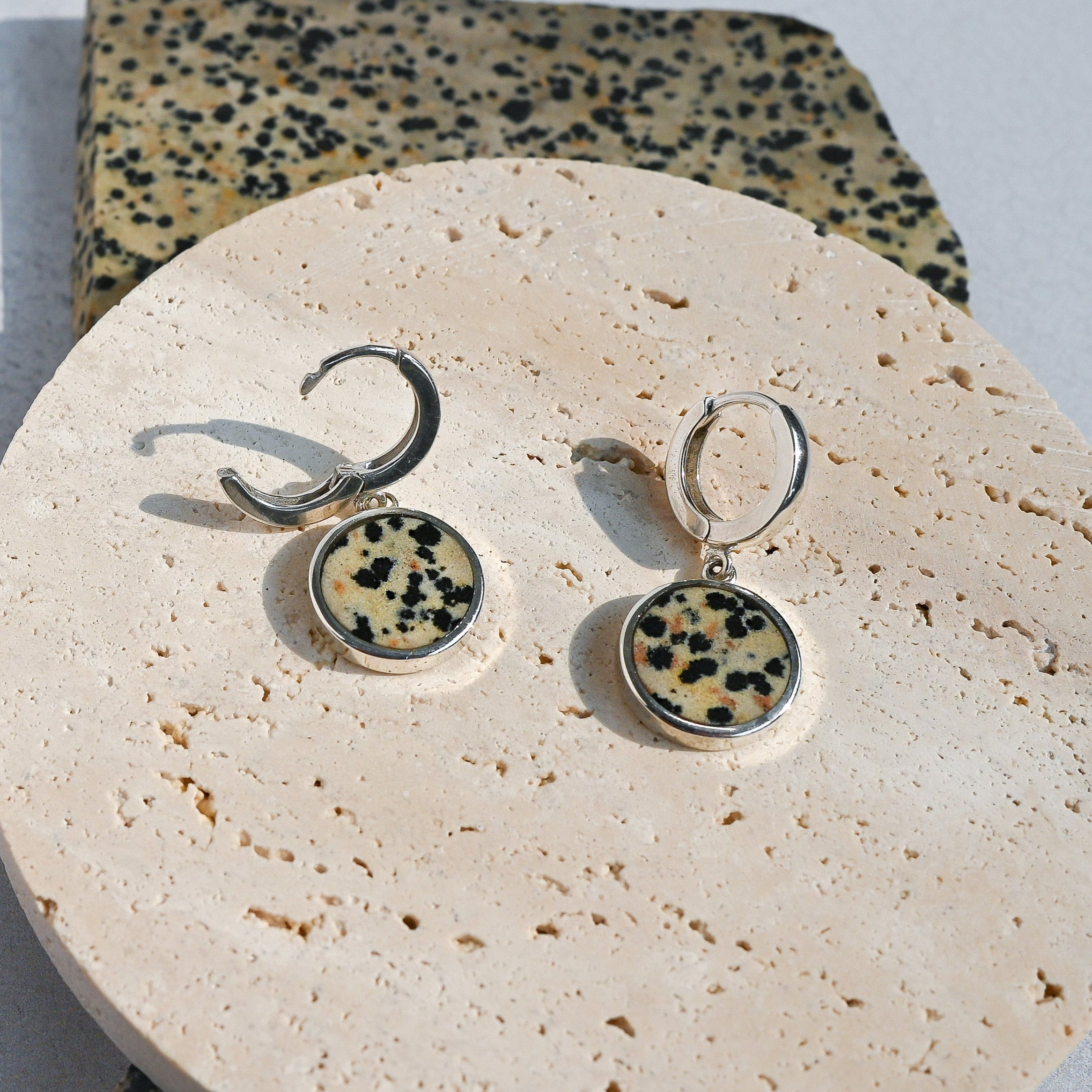 Pair of earrings with dalmatian jasper stones on a round stone surface.