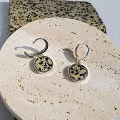 Pair of earrings with dalmatian jasper stones on a round stone surface.