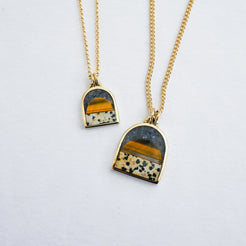 two gold pendant necklaces featuring a tiger's eye sun, a spotted dalmatian stone bottom and a dark blue lapis sky