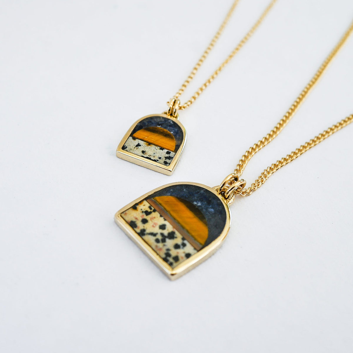 two gold pendant necklaces featuring a tiger's eye sun, a spotted dalmatian stone bottom and a dark blue lapis sky