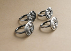Set of four silver rings with intricate designs on a beige background