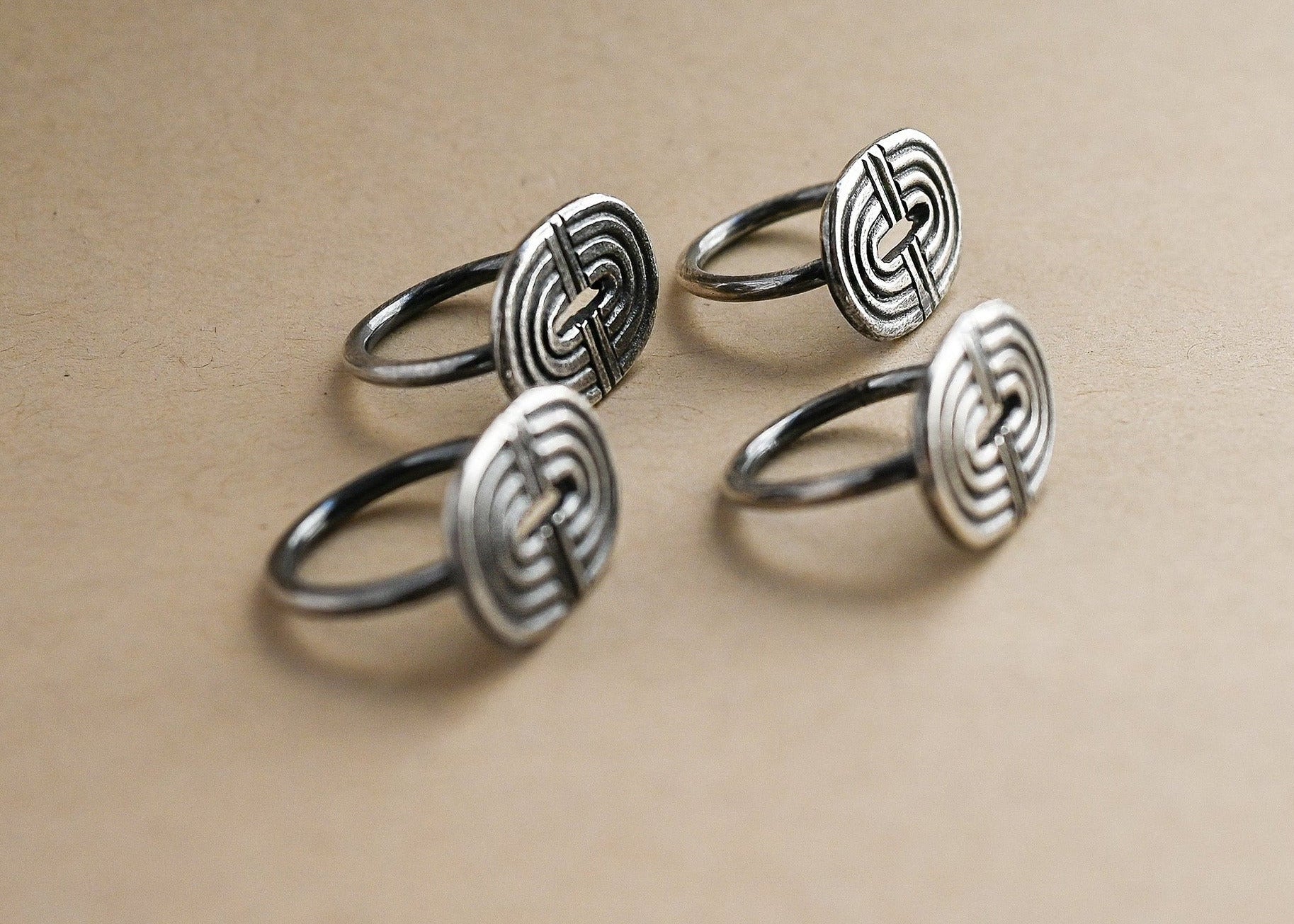 Set of four silver rings with intricate designs on a beige background