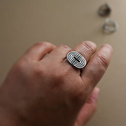 Hand wearing a silver ring with a geometric rainbow design on a neutral background
