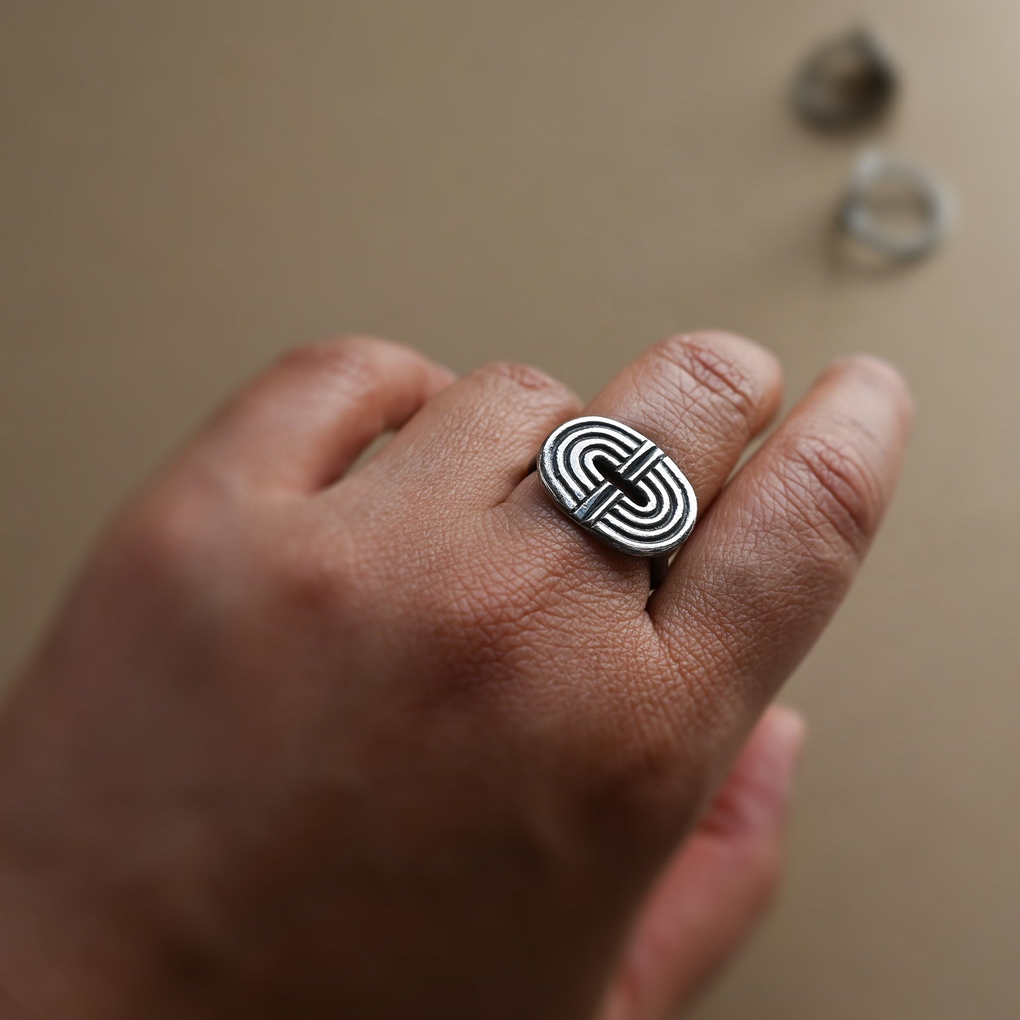 Hand wearing a silver ring with a geometric rainbow design on a neutral background