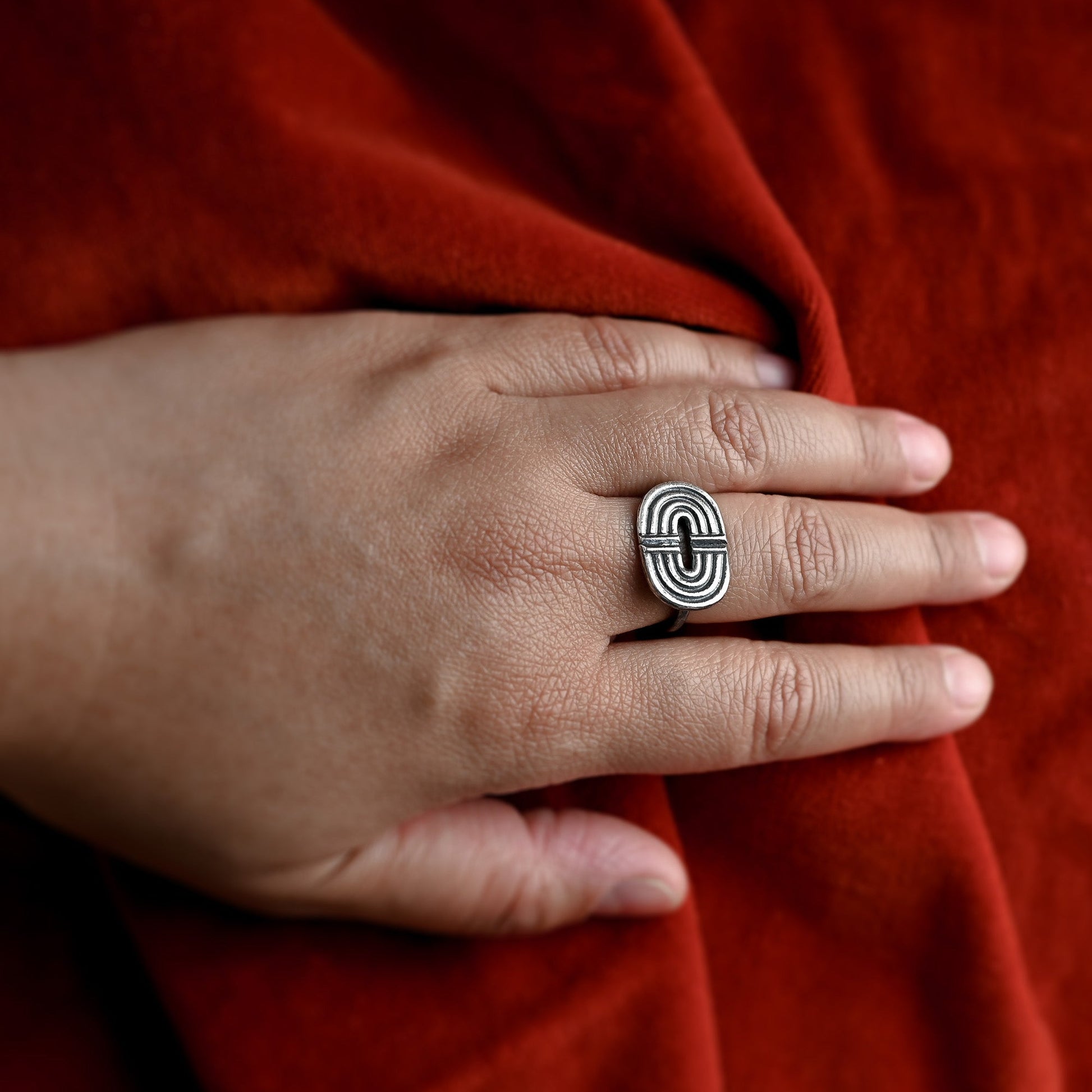 Hand wearing a silver ring with a red fabric background