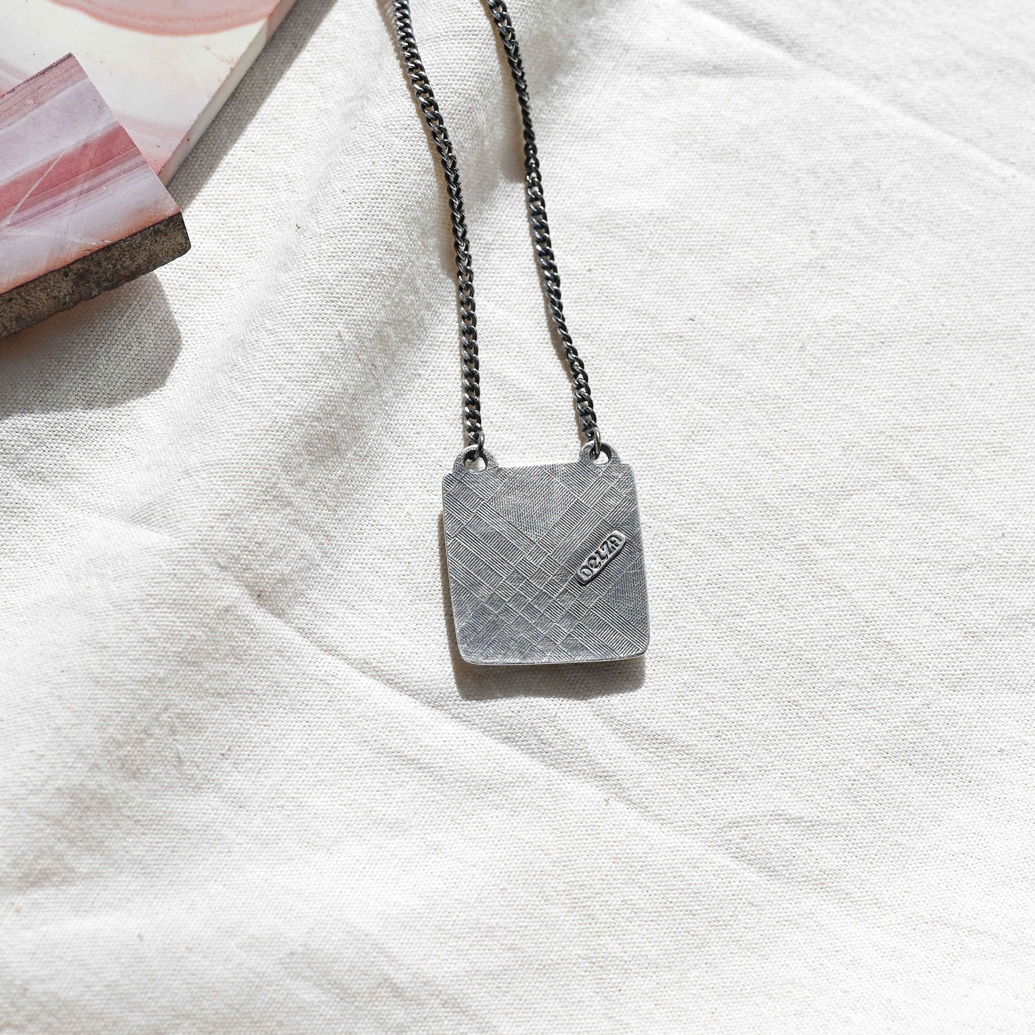 back of a silver pendant featuring a textured finish