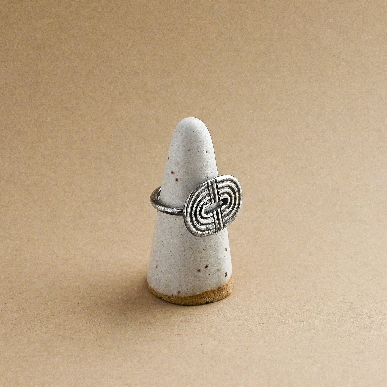 Silver ring with a rainbow design on a white ceramic ring form against a beige background