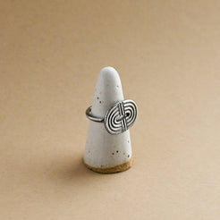 Silver ring with a rainbow design on a white ceramic ring form against a beige background