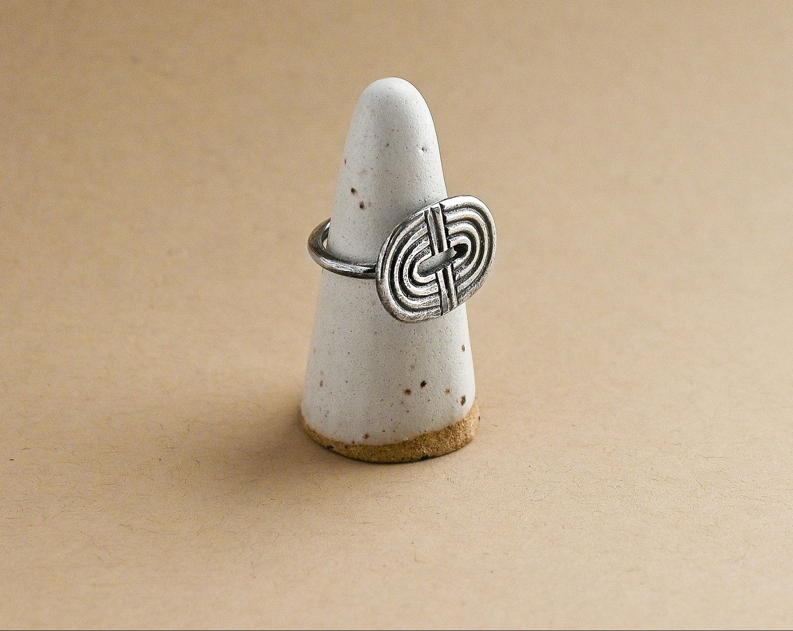 Silver ring with a rainbow design on a white ceramic ring form against a beige background