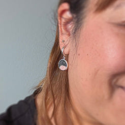 Close-up of a person wearing silver hoop earrings with pink and black elephant stone charms