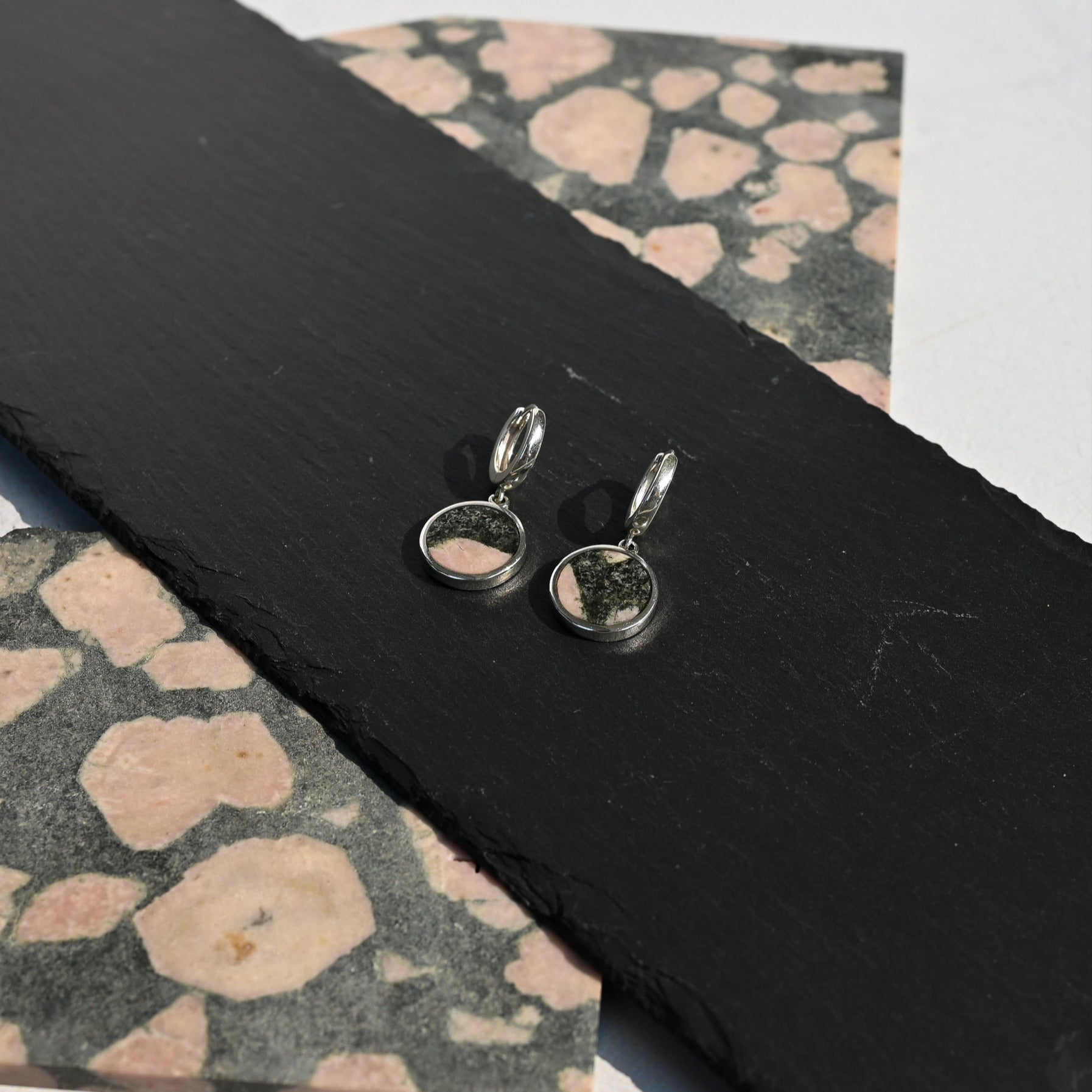 Silver hoop earrings with pink and black australian elephant stone charms on a dark slate surface