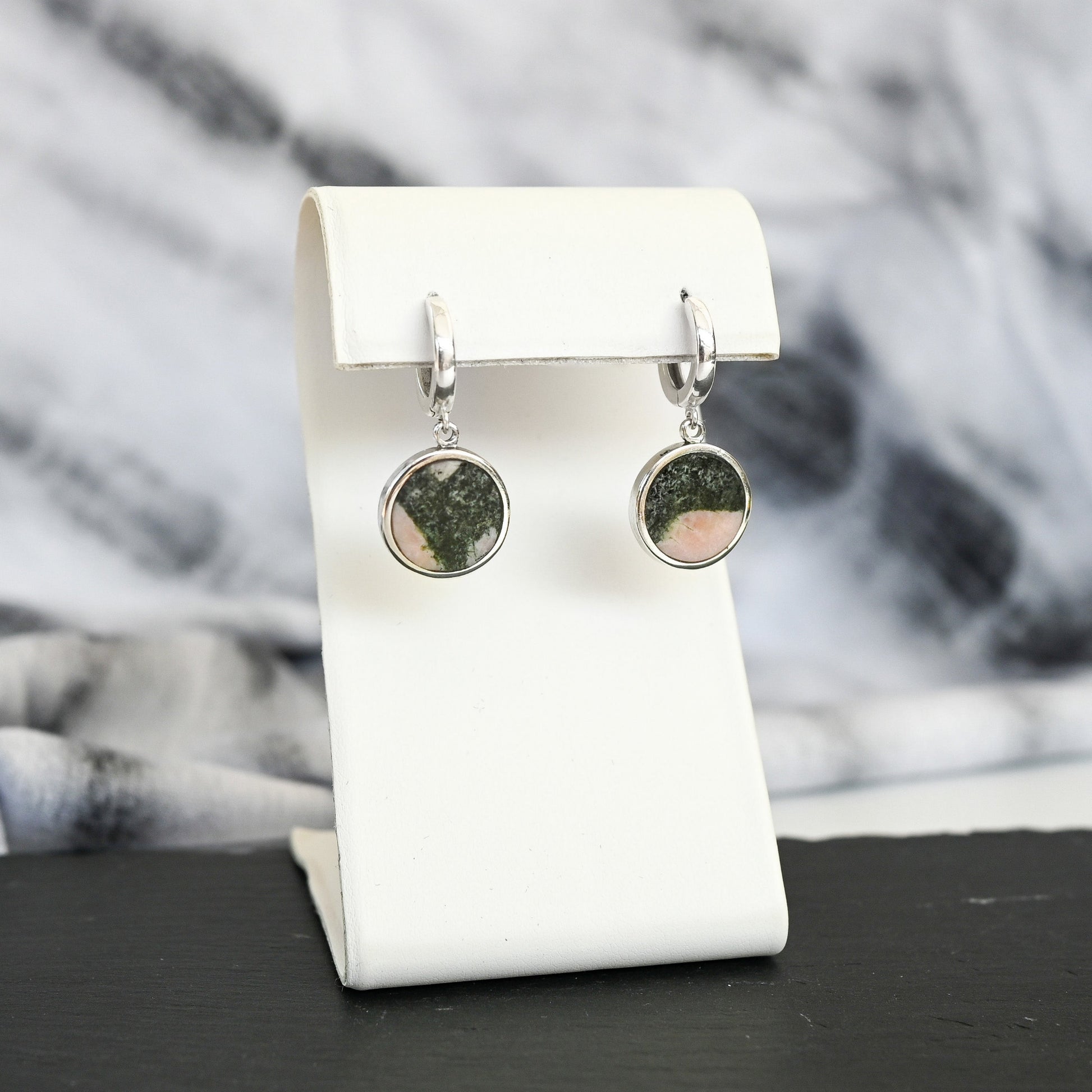 Pair of silver hoop earrings with pink and black australian elephant stone charms on a white stand with a blurred background