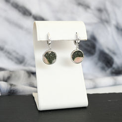 Pair of silver hoop earrings with pink and black australian elephant stone charms on a white stand with a blurred background
