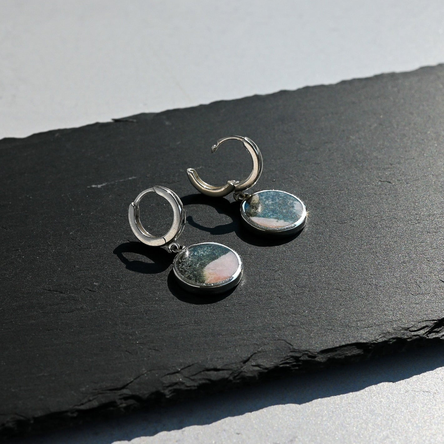 Pair of silver hoop earrings with pink and black elephant stone charm on a black slate surface