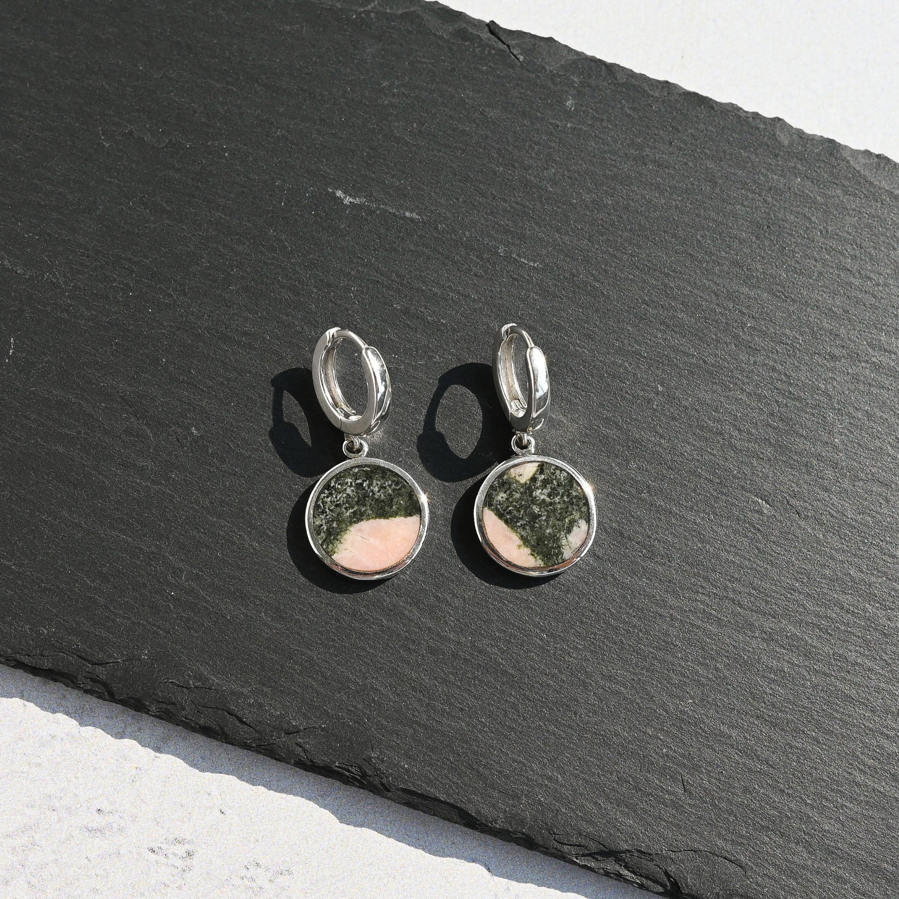 Silver hoop earrings with pink and black australian elephant stone charms on a dark slate surface