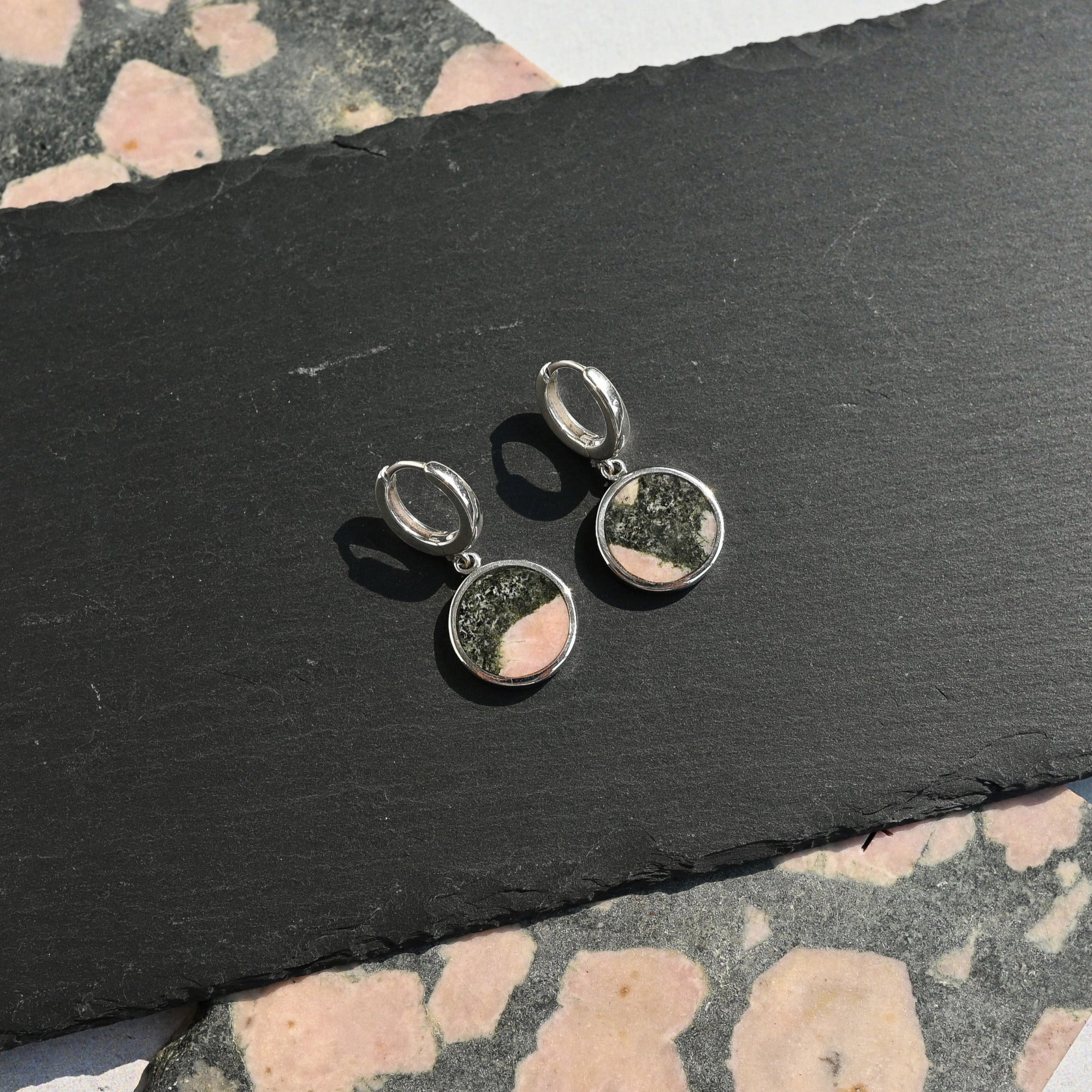 Pair of silver earrings with pink and black elephant stone on a black slate surface.