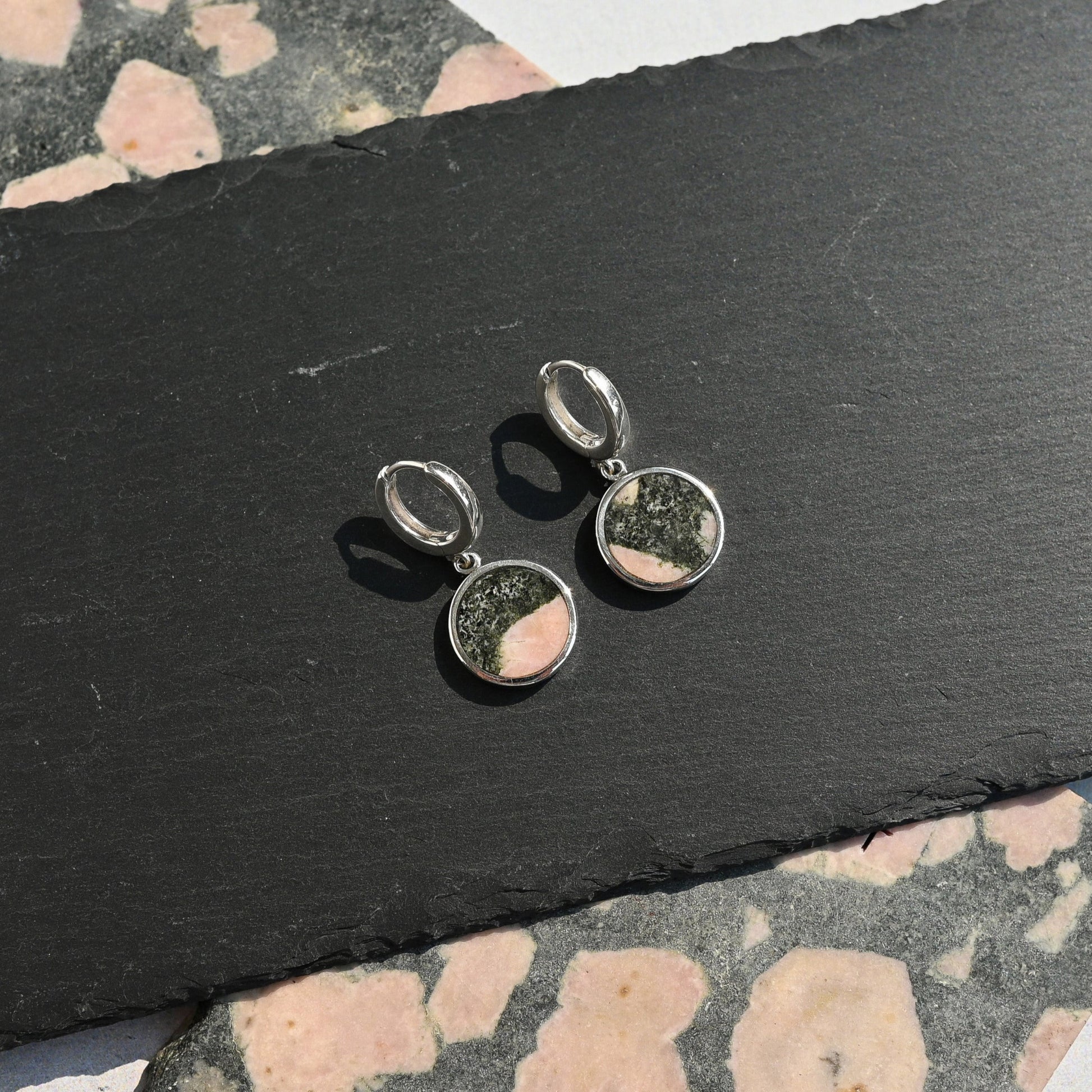Pair of silver earrings with pink and black elephant stone on a black slate surface.