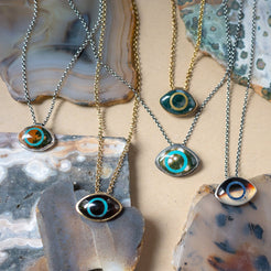 Five stone necklaces with eye-shaped pendants on a textured stone surface
