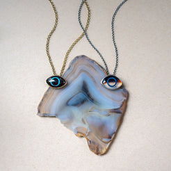two eye pendants, one in obsidian and one in montana agate, against an agate background