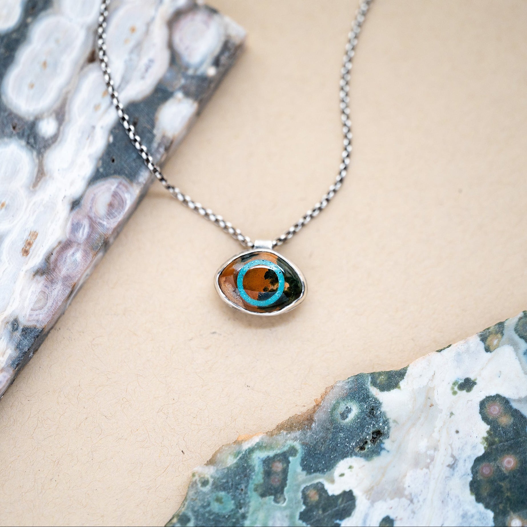 Necklace with an ocean jasper and turquoise eye pendant on a textured surface