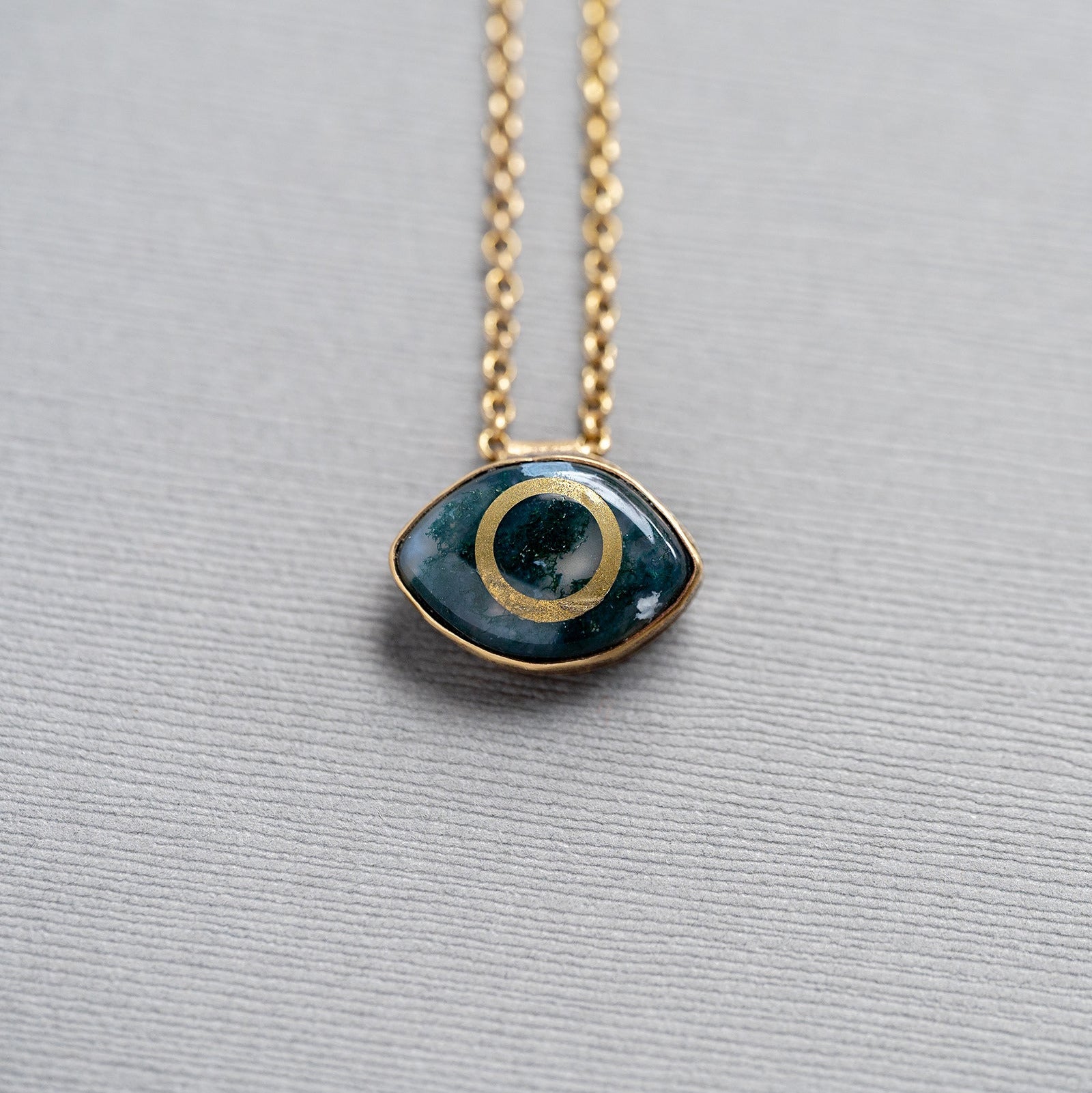 Necklace with a green moss agate eye-shaped stone pendant set in brass on a gray background